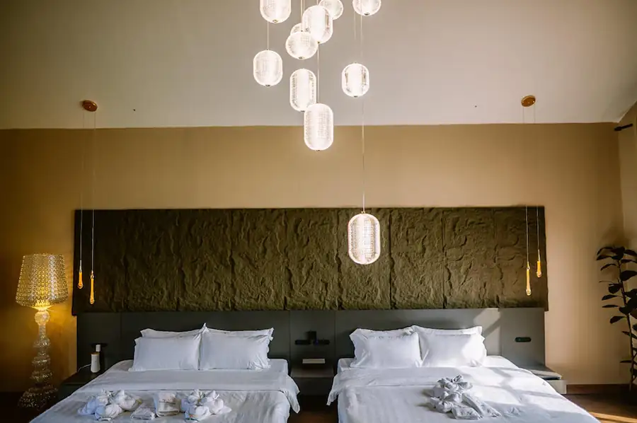 Two comfortable queen beds positioned against a textured stone accent wall beneath modern pendant lighting in the Bedroom Deluxe Two Queen Beds at Turtle Seaweed Resort.